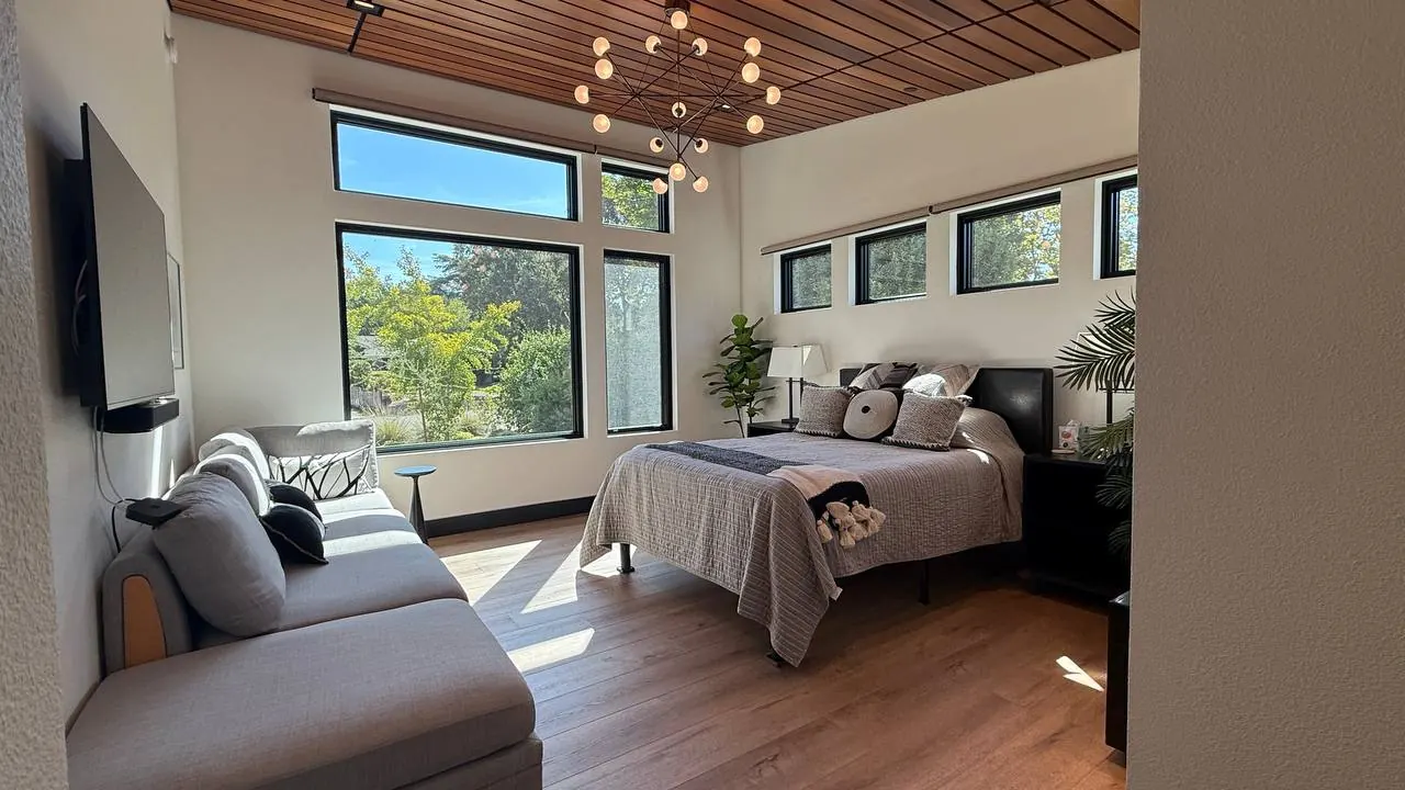 Bright, freshly cleaned bedroom with a made bed and large windows